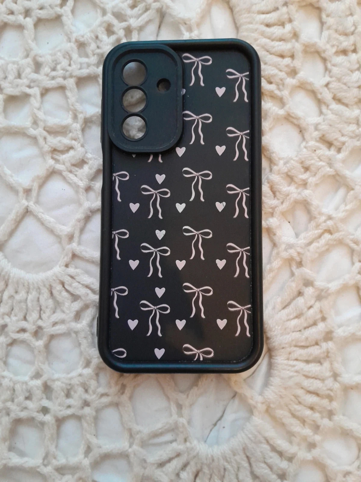 Coque de téléphone noire ornée d'un motif répétitif de petits nœuds et de cœurs blancs.